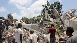 Menschen durchsuchen die Trümmer eines völlig zerstörten Hotels in Les Cayes. (Bild: APA/AFP/Stanley LOUIS)