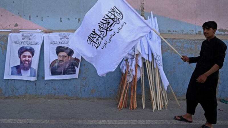 Ein Mann verkauft in Kabul Flaggen der Taliban. Die Poster neben ihm zeigen deren Anführer Amir Khan Muttaqi und Mullah Abdul Ghani Baradar. (Bild: APA/AFP/Aamir QURESHI)