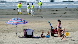 Ein skurriles Bild: Menschen sonnen sich am Strand, während Helfer unermüdlich gegen die Ölpest ankämpfen. (Bild: AP Photo/Ringo H.W. Chiu)