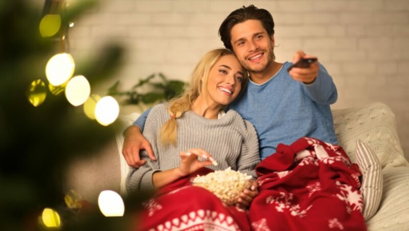 Loving couple watching tv at Christmas eve and eating popcorn at home (Bild: stock.adobe.com)