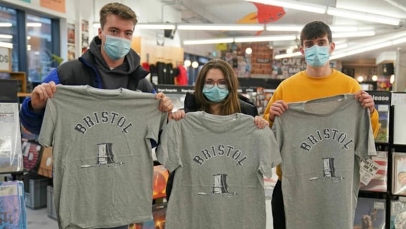 Kunden von Rough Trade in Bristol halten T-Shirts, die vom Straßenkünstler Banksy entworfen wurden. (Bild: APA/Jacob King/PA via AP)