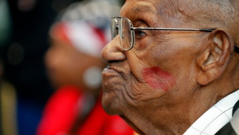 Lawrence Brooks wurde an seinem 110. Geburtstag von einer Sängerin der Gruppe Victoria Bells im Kriegsmuseum in New Orleans ein Lippenstiftküsschen auf die Wange gedrückt. (Bild: APA/AP Photo/Gerald Herbert)