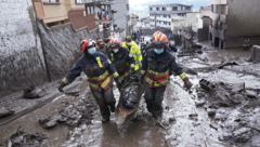 Rettungskräfte tragen eine Leiche weg, nachdem durch Regen ausgelöste Sturzfluten Bäche über die Ufer treten ließen und einen Hang zum Einsturz brachten. (Bild: Associated Press)