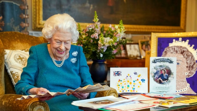 Queen Elizabeth liest sichtlich mit Vergnügen vor ihrem 70. Thronjubiläum noch einmal alte Glückwunschkarten und Andenken an zurückliegende Jubiläen. (Bild: APA/Steve Parsons/Pool via AP)