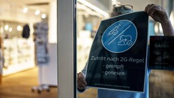 Eine Frau entfernt das 2G-Hinweisschild in einem Geschäft in Schleswig-Holstein. In dem deutschen Bundesland gilt die 2G-Regel schon jetzt nicht mehr, bald soll sie deutschlandweit fallen. (Bild: APA/dpa/Axel Heimken)