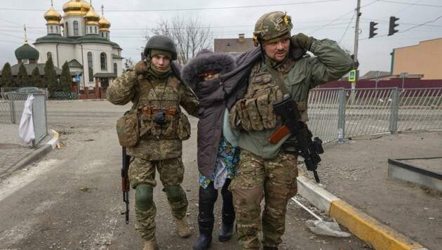 Ukrainische Soldaten helfen einer Frau im schwer bombardierten Irpin. (Bild: AP/Andriy Dubchak)