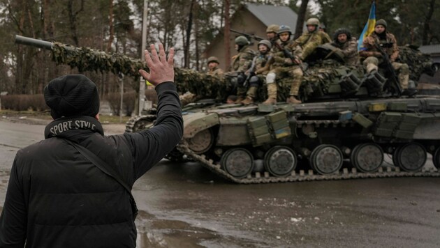 Ein Mann winkt ukrainischen Soldaten zu, die auf einem Panzer außerhalb von Kiew fahren. (Bild: The Associated Press)