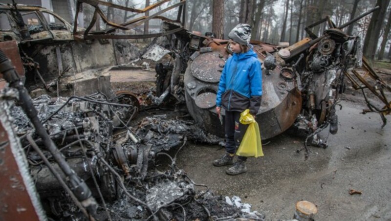 Ein Bub steht vor einem zerstörten russischen Panzer in Butscha. (Bild: AP)