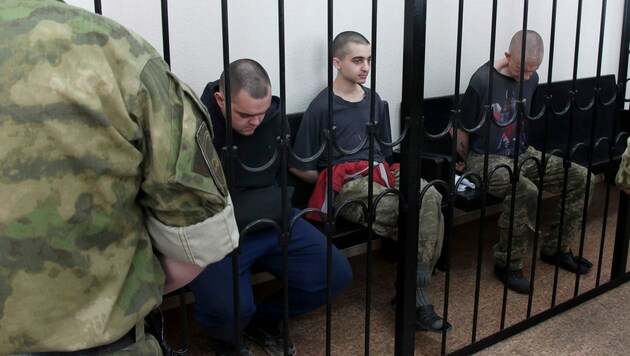 Die beiden britischen Staatsbürger Aiden Aslin (li.) und Shaun Pinner (re.) sowie der Marokkaner Saaudun Brahim (Mitte) sitzen hinter Gittern in einem Gerichtssaal in Donezk. (Bild: ASSOCIATED PRESS)