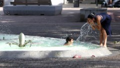 Ein Kind und ein Mädchen erfrischen sich an einem Brunnen und Teich in der Stadt Perpignan in Frankreich. (Bild: APA/AFP/RAYMOND ROIG)