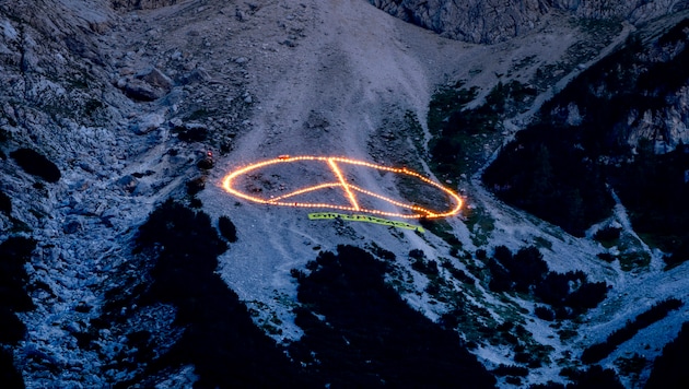 Greenpeace erregt Aufmerksamkeit beim G7-Gipfel: erst ein 60 Meter großes Peace-Zeichen aus brennenden Kerzen in einer Felswand bei Garmisch-Partenkirchen, dann ein Schriftzug am Waxenstein (Bild: Copyright 2022 The Associated Press. All rights reserved)