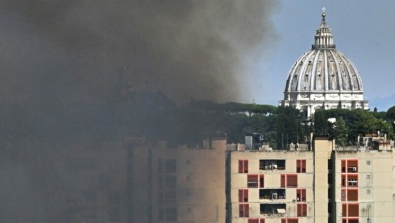 Nach einem Brand im Park Valle Aurelia in Rom am 4. Juli 2022 steigt Rauch aus der brennenden Vegetation auf, im Hintergrund ist die Vatikan-Kuppel zu sehen. (Bild: APA/AFP/Andreas SOLARO)