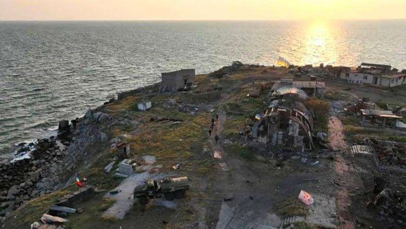 Inmitten von zurückgelassenem russischen Kriegsgerät weht die ukrainische Flagge im Ort Bile auf der Insel. (Bild: APA/AFP/Ukraine's border guard service/STR)