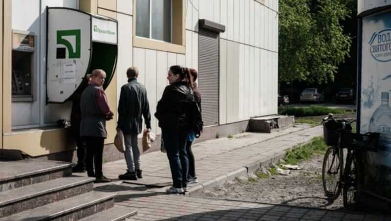 Menschen an einem Geldautomaten in der Ostukraine - Russland will in den besetzten Gebieten den Rubel einführen. (Bild: APA/AFP/Yasuyoshi CHIBA)