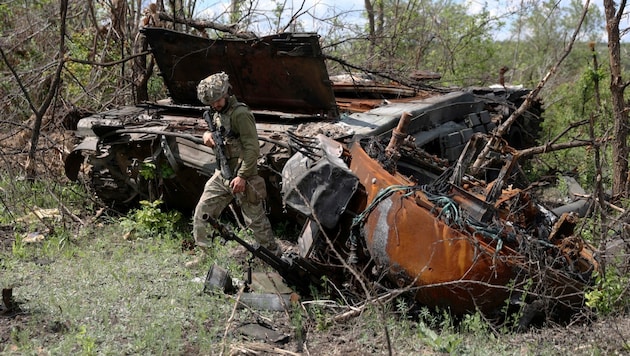 Ein ukrainischer Soldat inspiziert einen zerstörten russischen Panzer im Osten der Ukraine. (Bild: APA/AFP/Anatolii STEPANOV)