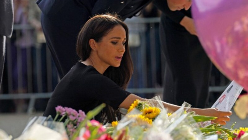 Herzogin Meghan begutachtet die Blumen und Schreiben im Gedenken an die Queen vor Schloss Windsor. (Bild: APA/Photo by Kirsty O‘Connor/AFP)