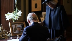 Camilla (re.) sieht zu, wie sich der britische König Charles III. während seines Besuchs in der königlichen Residenz Hillsborough ins Gästebuch einträgt. (Bild: AFP)