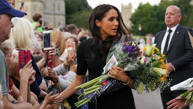 Herzogin Meghan hat den Arm bereits voller Blumen und will sich im ersten Moment nicht helfen lassen. (Bild: APA/Photo by Kirsty O‘Connor/AFP)