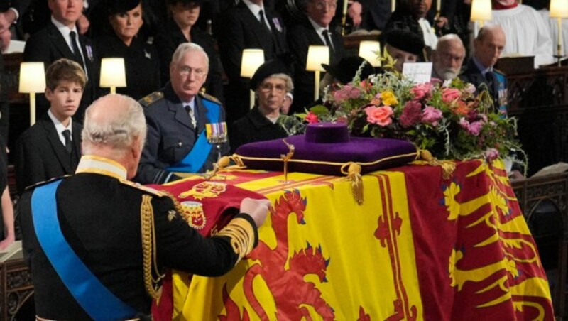 König Charles III. legt bei der Trauerfeier für die britische Königin Elisabeth II. in der St. George‘s Chapel auf Schloss Windsor die Kompaniefarbe der Grenadiergarde der Königin auf den Sarg, bevor er in die königlichen Gruft abgesenkt wurde. (Bild: APA/Photo by Jonathan Brady/AFP)