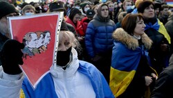 Bei einem Protest Anfang Februar gegen die bevorstehende russische Invasion hält eine Demonstrantin eine Karikatur von Putin, Stalin und Hitler hoch. (Bild: APA/AFP/Sergei SUPINSKY)