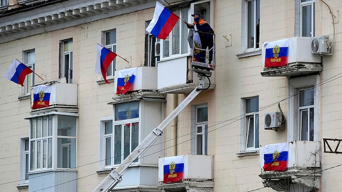 Archivbild aus dem Jahr 2022: Arbeiter beim Anbringen von russischen Flaggen an einem Wohnhaus ...