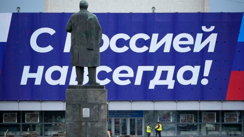 Eine Lenin-Statue schaut auf ein großes Plakat in den Farben Russlands mit der Aufschrift: „Russland für immer!“ in Luhansk. (Bild: AP)