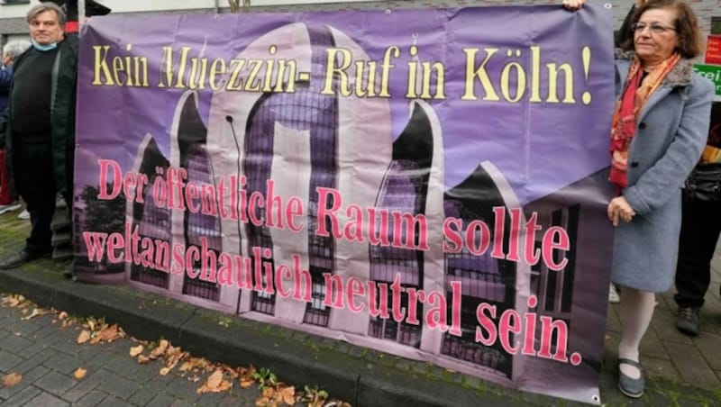 Menschen halten ein Transparent mit der Aufschrift „Kein Muezzinruf in Köln! Öffentlicher Raum soll ideologiefrei bleiben“ vor der Zentralmoschee in Köln (Bild: The Associated Press)