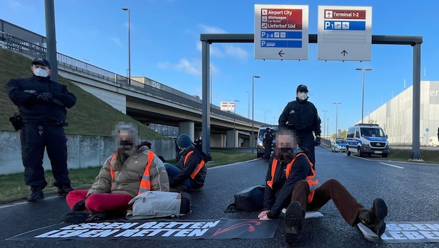 Im Februar blockierten Mitglieder der Gruppe „Letzte Generation“ die Zufahrt zu einem Flughafen (Bild). Am Montag lösten sie mit einer Aktion einen Stau aus, der auch ein Rettungsauto ausbremste. (Bild: APA/dpa/Paul Zinken, Krone KREATIV)
