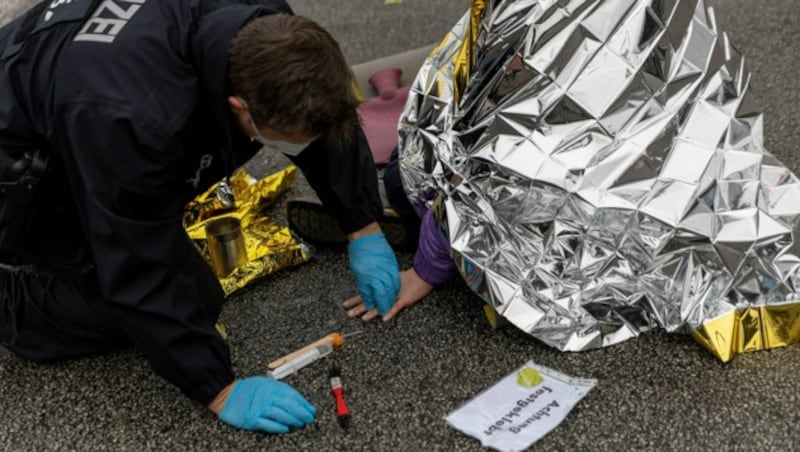 Ein Polizist löst im Februar 2022 mit einem Lösungsmittel den Klebstoff, mit dem sich ein Aktivist festgeklebt hat, von Hand und Fahrbahn. (Bild: APA/dpa/Carsten Koall)