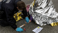 Ein Polizist löst im Februar 2022 mit einem Lösungsmittel den Klebstoff, mit dem sich ein Aktivist festgeklebt hat, von Hand und Fahrbahn. (Bild: APA/dpa/Carsten Koall)