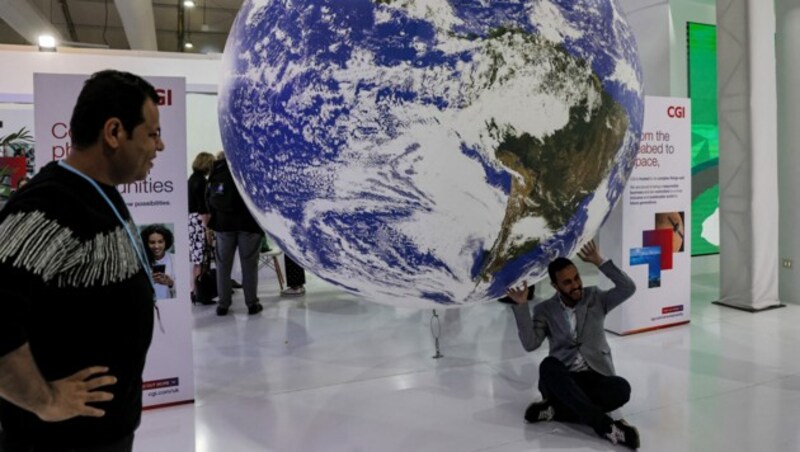 Ein Teilnehmer posiert für ein Foto unter einer Installation, die den Globus des Planeten Erde darstellt, während der COP27-Klimakonferenz im Scharm El-Scheich. (Bild: APA/AFP/AHMAD GHARABLI)