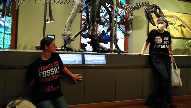 Jelena Saf (re.) und Caroline Thurner, Aktivistinnen der Letzten Generation, klebten sich im Naturhistorischen Museum Wien (NHM) an einem Dinosaurier-Podest fest. (Bild: APA/LETZTE GENERATION ÖSTERREICH)