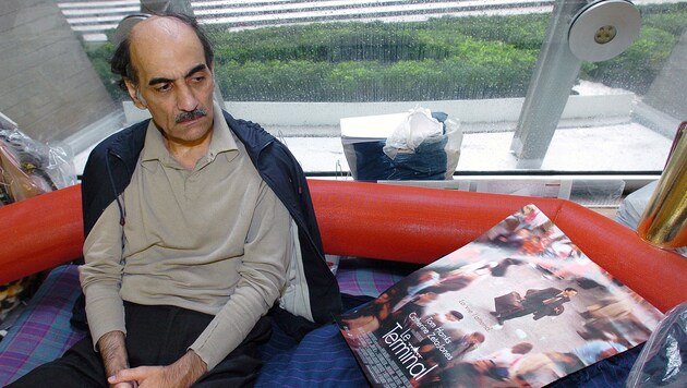 Mehran Karimi Nasseri mit einem Poster des Hollywoodfilms Terminal, der von ihm inspiriert wurde. (Bild: AFP)