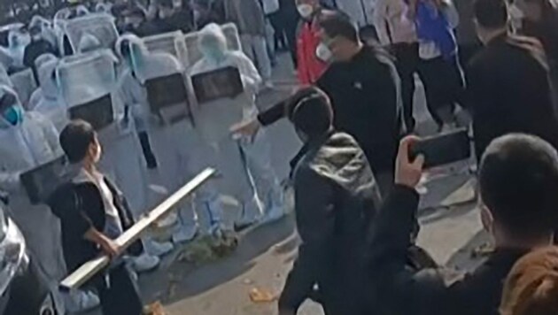 Dieses Bild aus einem AFP-Video vom 23. November 2022 zeigt Arbeiter in Foxconns iPhone-Fabrik in Zhengzhou, die mit Bereitschaftspolizisten und Personen in Schutzanzügen zusammenstoßen. (Bild: AFP)
