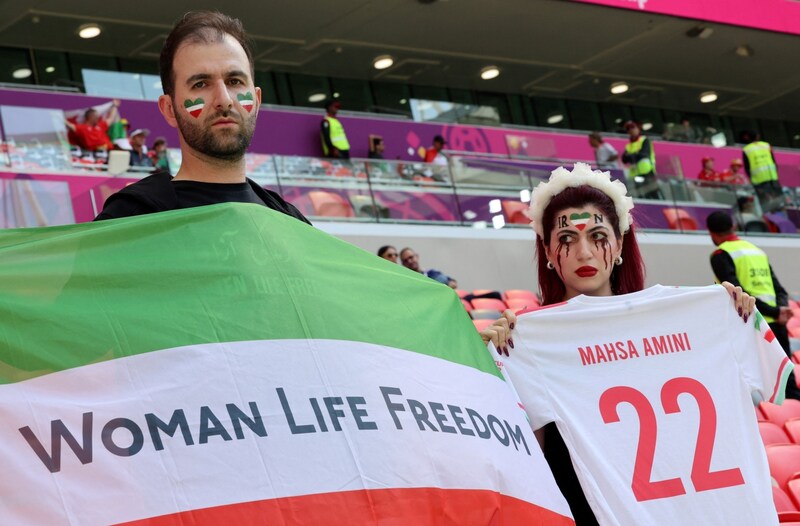 Eine iranische Anhängerin mit blutverschmiertem Gesicht hält ein Fußballtrikot mit dem Namen von Mahsa Amini in die Höhe. (Bild: AFP)