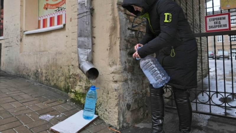 Eine Mitarbeiterin des Kiewer Gesundheitsamtes sammelt Regenwasser aus einem Abflussrohr in Kiew. (Bild: AP)