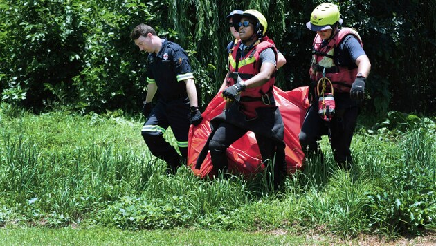 Retter tragen die Leiche eines Überschwemmungsopfers, das aus dem Fluss Jukskei in Johannesburg geborgen wurde. (Bild: The Associated Press)