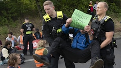 Berlin: Polizeibeamte tragen einen Demonstranten der Gruppe „Letzte Generation“ von einer Fahrbahn (Archivbild) (Bild: APA/dpa/Paul Zinken)