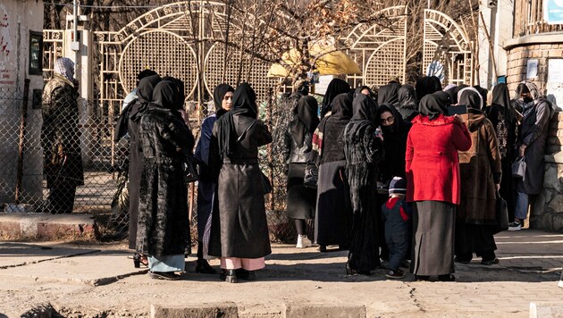 Afghanische Universitätsstudentinnen stehen am Mittwoch vor einer Universität in Kabul und werden von Taliban-Sicherheitskräften aufgehalten. (Bild: APA/AFP/Wakil KOHSAR)