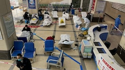 Ein Mann steht vor einem abgesperrten Bereich, in dem Corona-Patienten auf Krankenhausbetten liegen. (Bild: AFP)