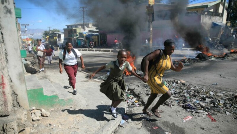 Eine Frau und ihre Tochter rennen an einer Barrikade vorbei, die von Polizisten in Haiti errichten wurden. (Bild: Associated Press)