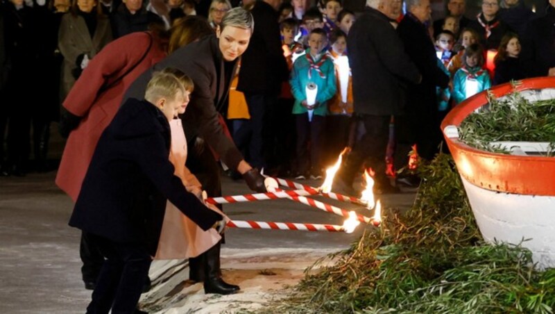 Fürstin Charlène von Monaco und ihre Kinder Fürst Jacques und Fürstin Gabriella zünden während der traditionellen Feierlichkeiten des Feiertages Sainte Devote im Fürstentum Monaco ein Segelboot an. (Bild: APA/Photo by ERIC GAILLARD/AFP)