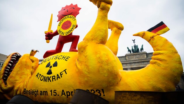 Die rote Sonne, Teil des Anti-Atomkraft-Logos, steht bei einer Aktion der Umweltorganisation Greenpeace vor dem Brandenburger Tor auf einer Dinosaurier-Figur, um die Abschaltung der letzten drei deutschen Kernkraftwerke zu feiern. (Bild: APA/dpa/Christoph Soeder)