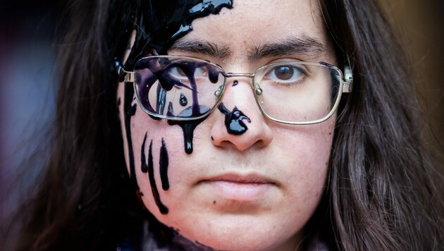 Eine Aktivistin der Klimagruppe Letzte Generation hat vor der FDP-Bundesgeschäftsstelle ölartige Farbe im Gesicht. (Bild: APA/dpa/Christoph Soeder)