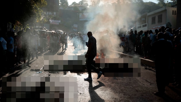 Schaulustige begutachten die verkohlten Leichen der mutmaßlichen Bandenmitglieder. (Bild: AP, Krone KREATIV)