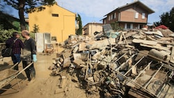 Freiwillige beseitigen Schlamm, während Haushaltsgegenstände am Straßenrand in Faenza - in der vom Hochwasser betroffenen Region Emilia Romagna - liegen. (Bild: AP)