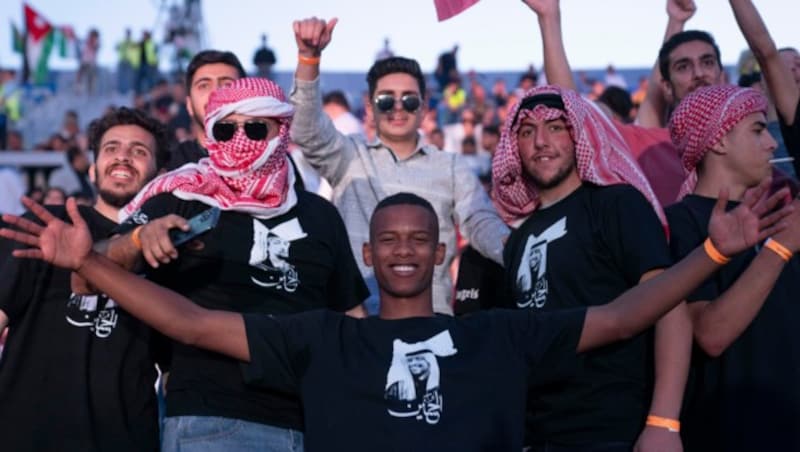 Jordanische Männer, die das traditionelle rot-weiß-karierte jordanische Halstuch und T-Shirts mit Bildern des jordanischen Kronprinzen Hussein tragen, tanzen und singen bei einem Konzert in einem Sportstadion in Amman. (Bild: Nasser Nasser / AP / picturedesk.com)