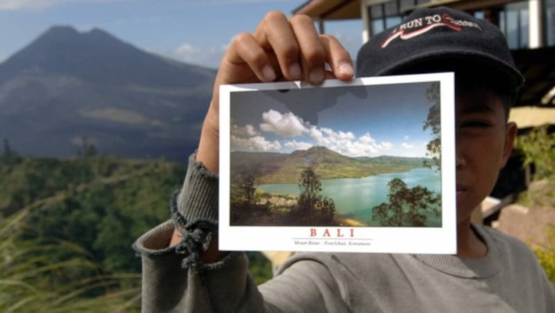 Ein Verkäufer mit einer Ansichtskarte, die den bei Touristen sehr beliebten Mount Batur zeigt (Bild: AFP/Sonny Tumbelaka)