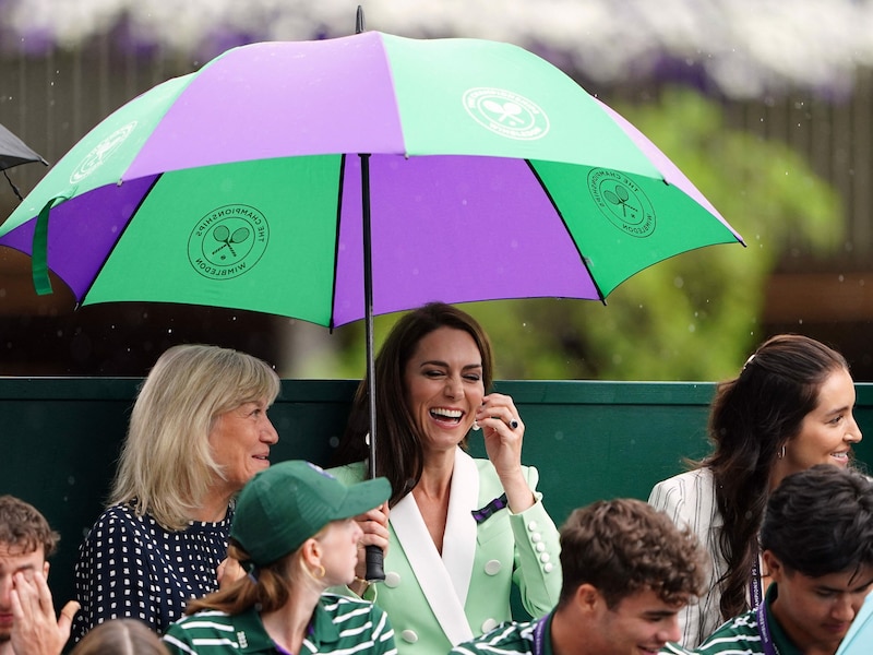 Kate teilt sich mit den ehemaligen Tennisspielerinnen Deborah Jevans (l.) und Laura Robson (r.) Schirm. (Bild: APA/AFP/POOL/Zac Goodwin)