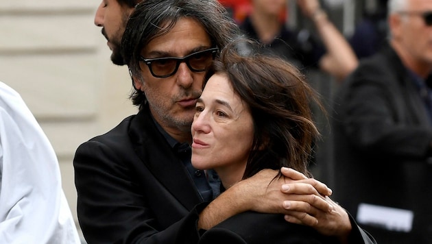 Der Fotograf fing ein, wie Birkins ältere Tochter Charlotte Gainsbourg von ihrem Ehemann Yvan Attal getröstet wird. (Bild: APA/AFP/JULIEN DE ROSA)